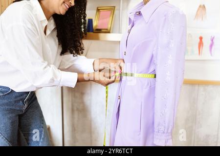 Creative seamstress measures waist of lavender dress in stylish office Stock Photo