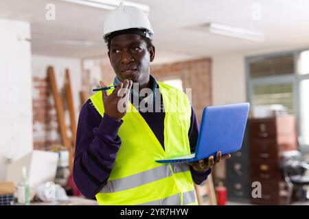 Man construction worker with laptop talking ob phone inside apartment Stock Photo