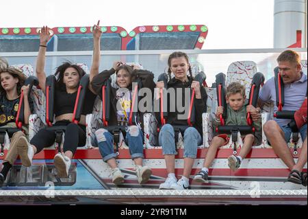 Engure, Latvia, July 8, 2023: A group of excited children and adults sit strapped in on a ride Stock Photo