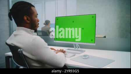 Professional African American financial expert or marketing specialist works on personal computer with green screen chromakey. Mock up template for screen content. Modern office of E-commerce company. Stock Photo