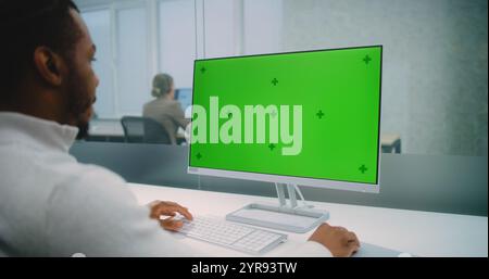 Professional African American financial expert or marketing specialist works on personal computer with green screen chromakey. Mock up template for screen content. Modern office of E-commerce company. Stock Photo