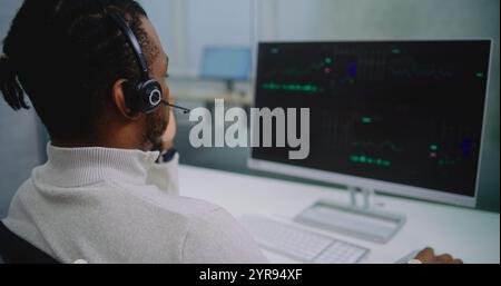 African American professional financial specialist in headset analyzes share market and stocks on computer. PC screen shows charts and diagrams. Modern office of stock exchange company. E-business. Stock Photo