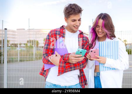 Young students smiling and using smartphones with colorful notebooks outdoors Stock Photo
