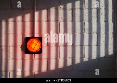 A red wall lamp on a brick wall with a patterned shadow Stock Photo