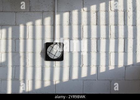 A wall lamp on a brick wall with a patterned shadow Stock Photo