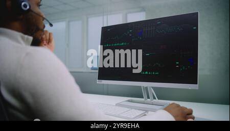 African American man works in modern office of international company: Stock exchange trader talks on headset, monitors equity market and shares using computer, analyzes charts and diagrams. E-commerce Stock Photo