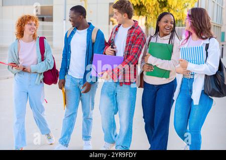Group diverse students walking together with notebooks outdoors on a sunny day Stock Photo