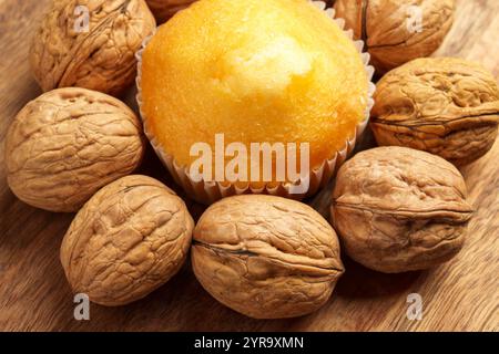 A close-up of fresh golden muffin surrounded by unshelled walnuts on rustic wooden surface. High calorie energy packed snack combines richness and nut Stock Photo
