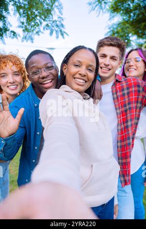 Happy diverse group of friends taking a selfie outdoors, smiling and waving Stock Photo