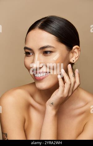 Brunette woman smiles warmly while applying makeup against a neutral backdrop. Stock Photo