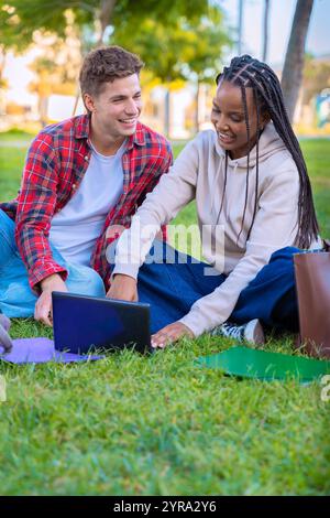 Young couple using laptop together while sitting on grass outdoors.Vertical Stock Photo