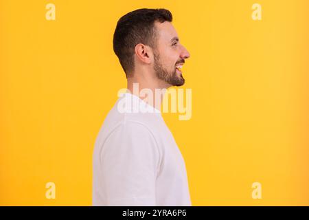 Side view Portrait of a smiling man in white t-shirt against yellow background. Stock Photo