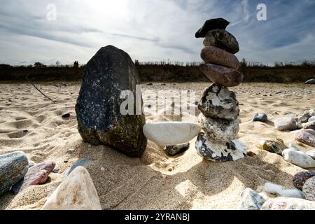 White balanced stone between arranged natural stone piles at the sandy beach of the Baltic Sea depicting harmony and a calm and balanced life style Stock Photo