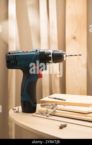 A cordless electric drill is prominently displayed on a workbench, accompanied by screws, drill bits, and wooden planks, highlighting its essential ro Stock Photo