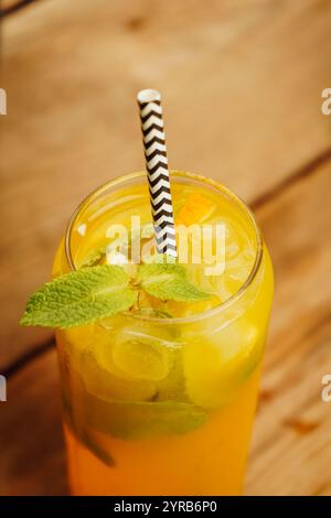 A glass of iced lemonade shines with slices of citrus and delicate leaves of herbs, contrasting beautifully against a dark background. A visual and Stock Photo