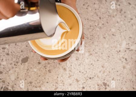 Latte art. Barista standing near the counter pouring frothed milk in a small cup of cappuccino. Stock Photo