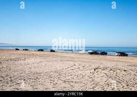 Cars parked along the sandy shoreline of a California beach, with ocean waves and clear blue skies in view. Stock Photo