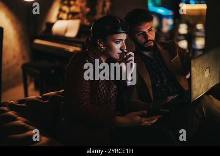 Two people collaborating intensely on a laptop in a cozy setting Stock Photo