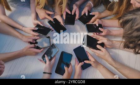 People holding their smartphones around a white table, using their devices and showing a sense of community. Stock Photo