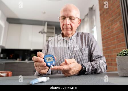 Man is taking his blood sugar reading. He is wearing glasses and is sitting at a table Stock Photo