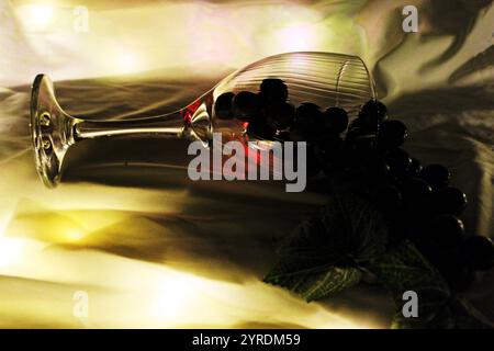 Representation of a glass of wine fallen on the table, staining the tablecloth; the grapes symbolize wine. Stock Photo