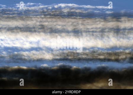 High cirrus clouds lit from a low sun are arranged in ethereal plains like waves in the sky Stock Photo