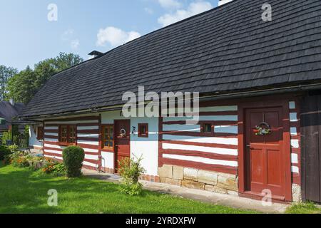 Traditional half-timbered house with red and white stripes and a well-tended garden under a blue sky, Old wooden house, Vesec u Sobotky, village conse Stock Photo