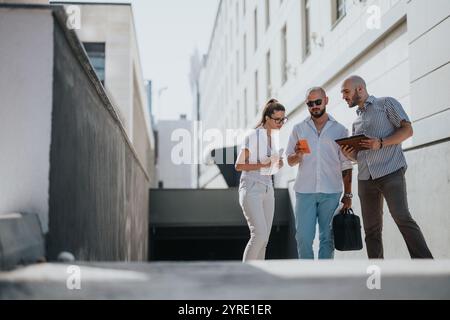 Business team collaborating outside modern office building while using digital devices Stock Photo