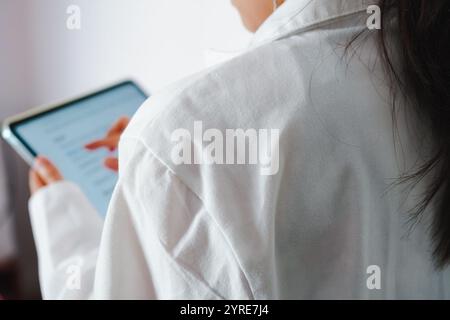 Close-up of the back of a young female doctor checking patient information on a tablet Stock Photo