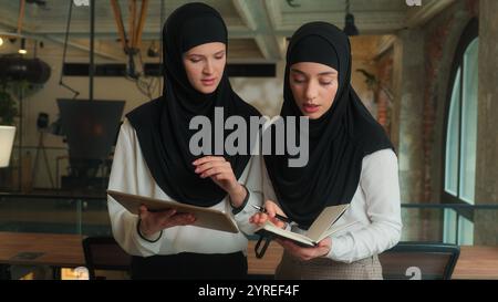 Two muslim women in hijab business partners Arabian girls students female team coworkers colleagues discuss online project on computer tablet islamic Stock Photo