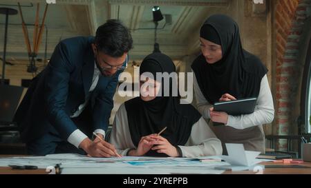 Arabian business man muslim women in hijab teamwork architecture paperwork multiethnic male female help intern drawing building plan in office Stock Photo