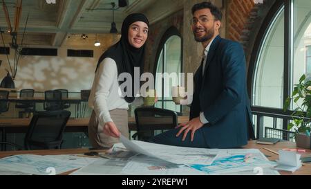 Happy male female business partners Arabian Indian man businessman Muslim woman hijab businesswoman architects designers drink coffee discuss building Stock Photo