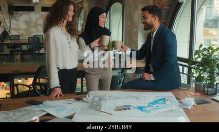 Team architects contractors engineers business colleagues Arabian Muslim Caucasian businessman businesswomen drink coffee break happy relaxed man Stock Photo