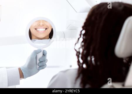 Beautiful young black woman looking at mirror in dentists office Stock Photo