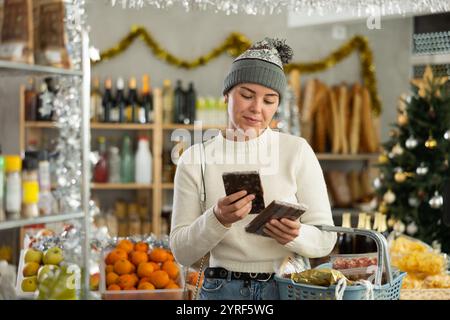 Smiling girl choosing chocolate in grocery store with Christmas decorations Stock Photo