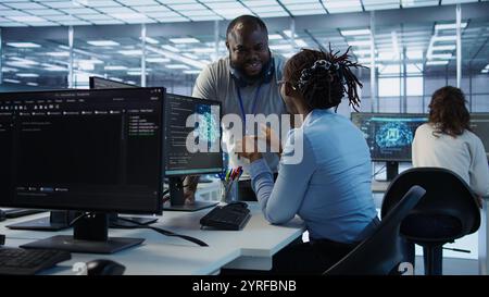 Manager doing team meeting with engineers, delegating tasks in high tech data center office. Supervisor doing brainstorming with IT experts how to while monitor AI supercomputers, camera B Stock Photo