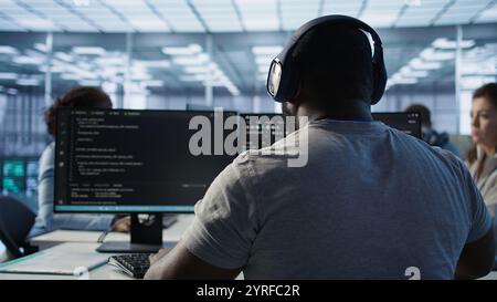 System administrator working in computer network security data center listening music. African american worker wearing headphones monitoring server racks energy consumption, camera B Stock Photo