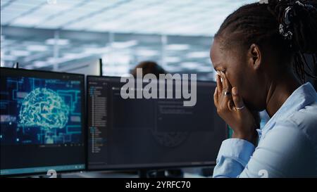 Tired software developer having eye strain while working on high tech data center computer. Overworked african american woman removing glasses to relax eyes in server room, camera B close up Stock Photo
