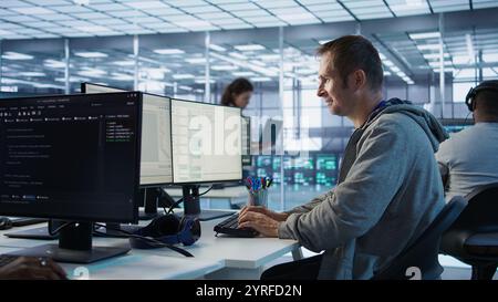 Man working in server hub capable of processing vast amounts of data. IT programmer at PC desk typing on keyboard, updating servers controlling network resources, camera B Stock Photo