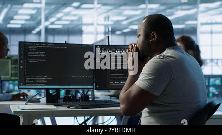 Admin working in computer network security data center suffering from cold, sneezing. Ill african american worker coughing while monitoring server racks, coming up with flu, camera A Stock Photo