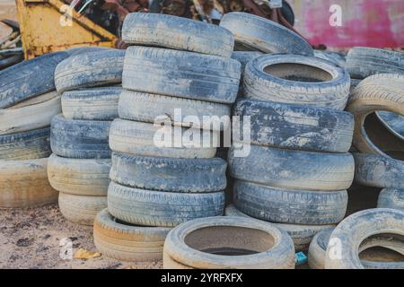 A large pile of used tires stacked on top of each other. The tires are weathered and show signs of wear and tear. Stock Photo