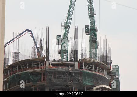 A working day at the construction site. Workers in the heights, steel beams, cranes, and cables. Photo taken on a sunny day. Stock Photo