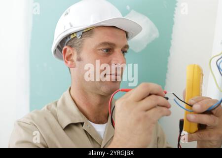 happy electrician checking voltage in electrical wall socket Stock Photo