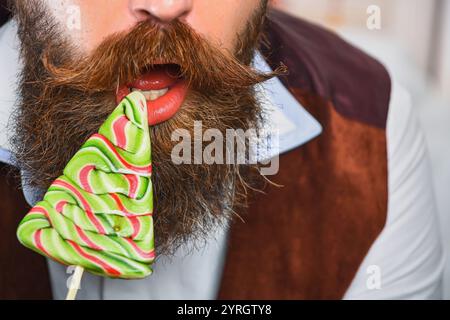 Xmas holiday celebration. Bearded man at New Year eve. December holiday party for man having moustache. Xmas man eating candy lollipop. Christmas Stock Photo