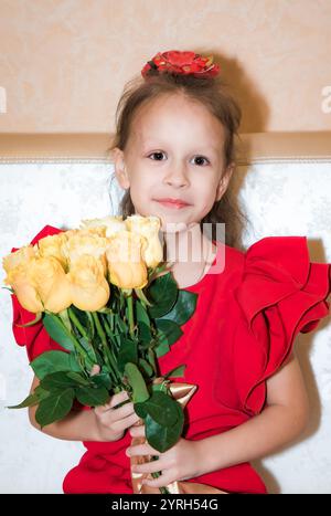 An 8-year-old Russian girl in a red outfit holds a bouquet of yellow roses, celebrating her birthday. She looks at the camera with a sweet expression, Stock Photo