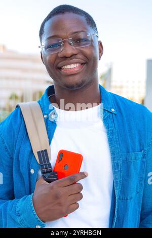 Smiling young man holding smartphone and notebooks outdoors in casual attire Stock Photo