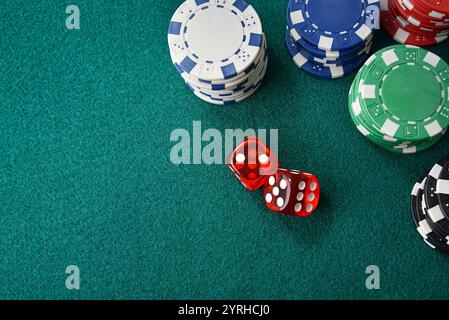 Casino dice game background with stack of colored chips for betting and two red dices around on green felt table. Top view. Stock Photo