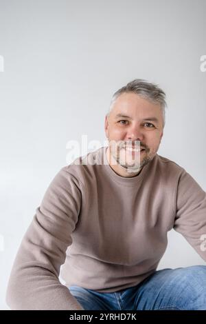 Portrait of a friendly, middle-aged man with a warm smile. He s dressed casually in a taupe sweatshirt and jeans, creating a relaxed and approachable Stock Photo