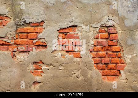 badly damaged and crumbling render on red brick wall, rendering falling from a wall, red brick wall covered in crumbling mortar render. Stock Photo