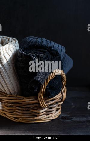 A wicker basket filled with neatly folded knitted garments in various colors against a dark background Perfect for themes of comfort, warmth, and home Stock Photo